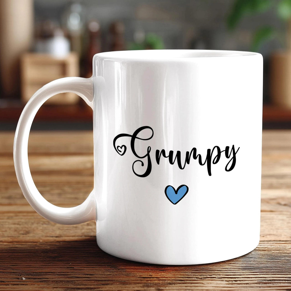 A white ceramic mug with the word "Grumpy" written on it in a cursive font, along with a small blue heart symbol.