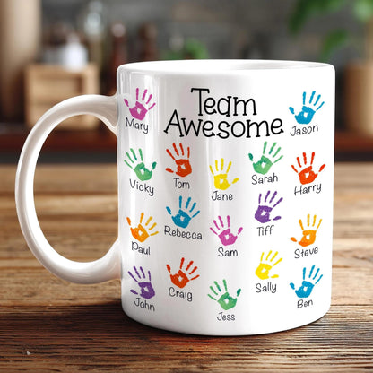 A white mug with colorful handprints on it, each containing a name.