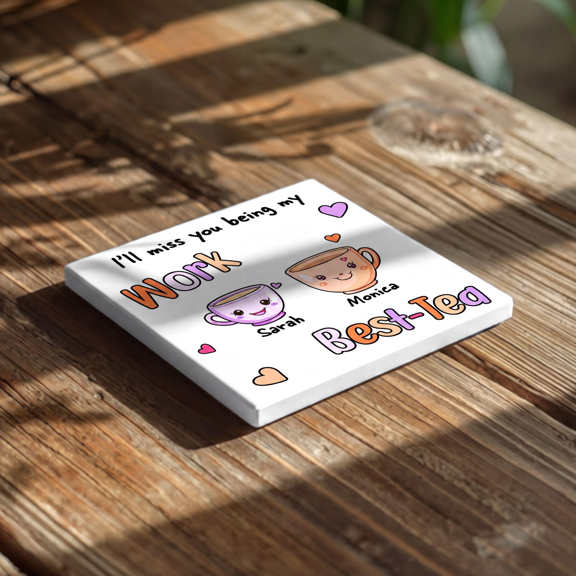 A white square coaster with a message about missing someone and a cartoon image of two cups of tea.
