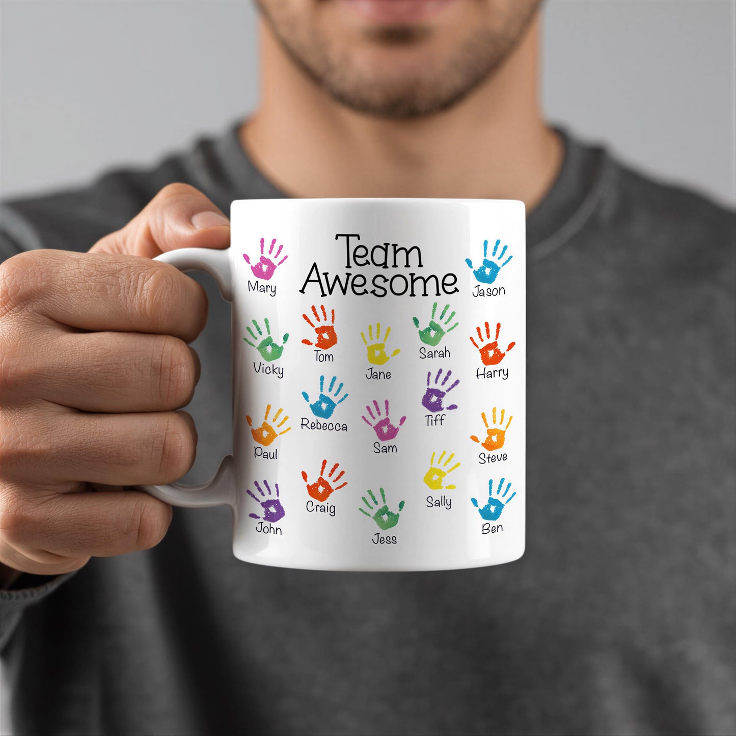 A person is holding a white mug with colorful handprints on it, each representing a different person's name.