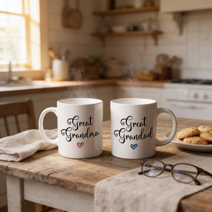 Two white mugs with the text "Great Grandma" and hearts printed on them, placed on a wooden table in a kitchen setting.
