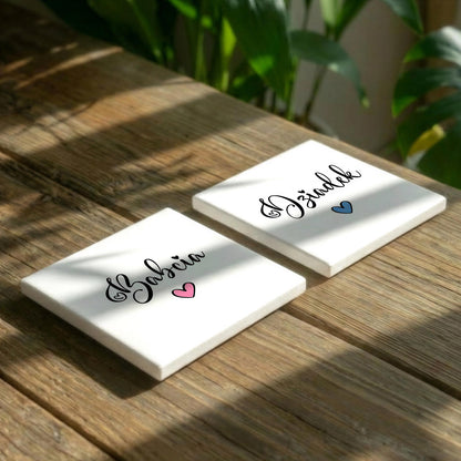Two white square coasters with the name "Gazebo" written on them, placed on a wooden surface with a plant in the background.