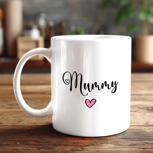 A white ceramic mug with the word "Mummy" written on it, along with a pink heart symbol, sits on a wooden surface.