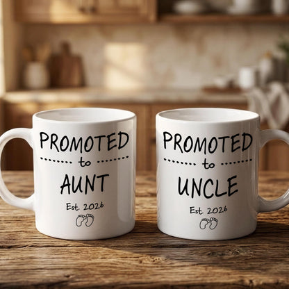 Two white mugs with black text that reads "PROMOTED TO AUNT Est. 2026" and "PROMOTED TO UNCLE Est. 2026" printed on them.