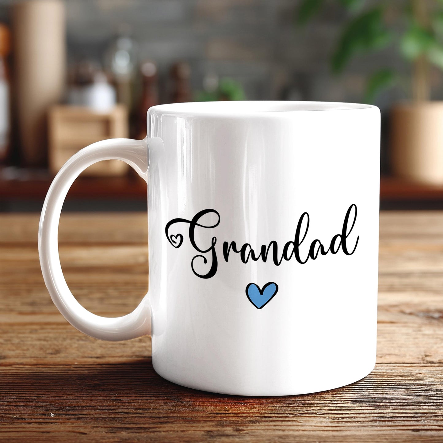A white ceramic mug with the text "Grandad" and a blue heart symbol printed on it, placed on a wooden surface.