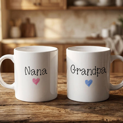 Two white mugs with the names "Nana" and "Grandpa" printed on them, along with a heart symbol, are placed on a wooden surface.