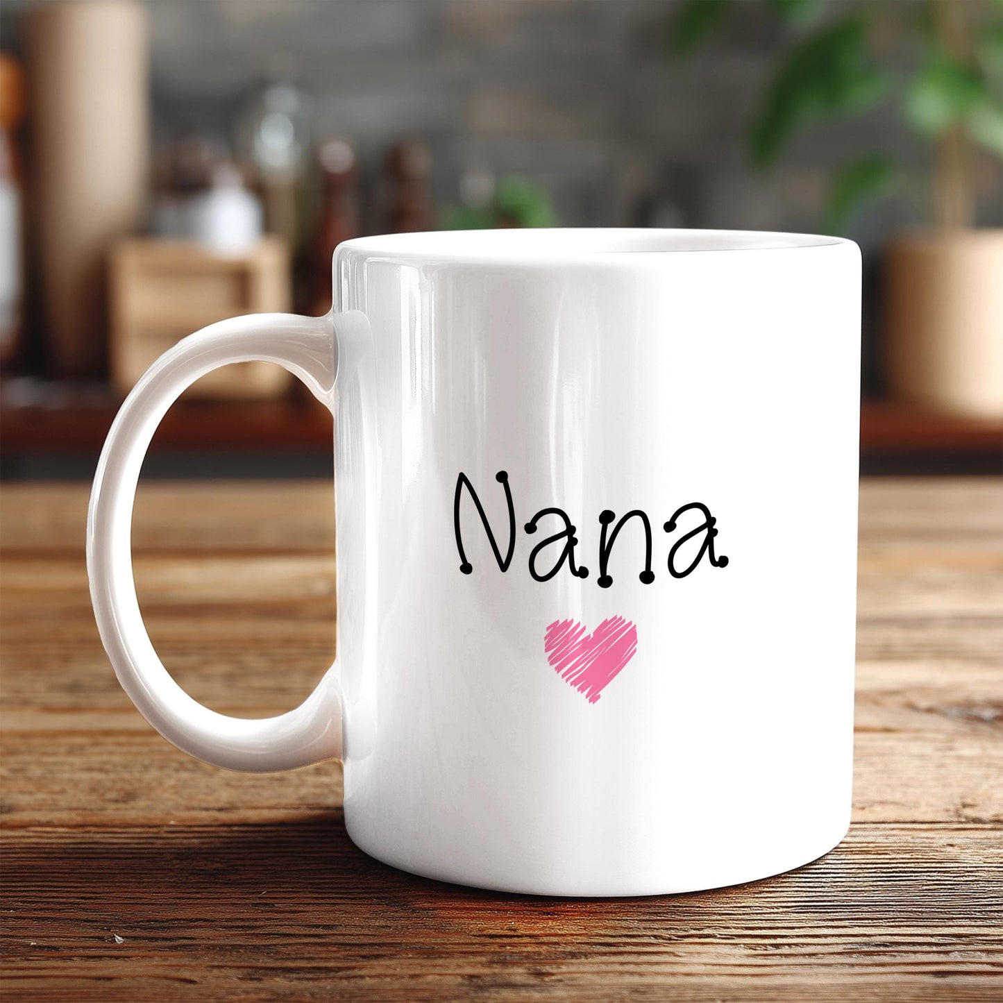 A white ceramic mug with the word "Nana" and a pink heart printed on it, placed on a wooden surface.