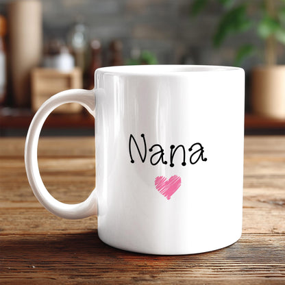 A white ceramic mug with the word "Nana" and a pink heart printed on it, placed on a wooden surface.