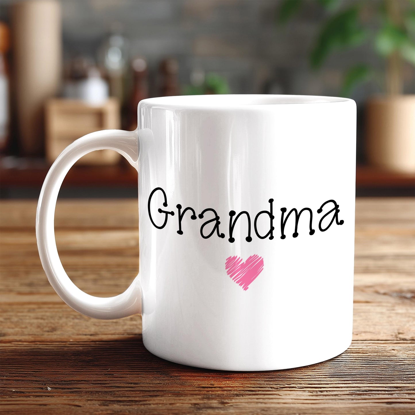 A white ceramic mug with the word "Grandma" written on it, along with a pink heart symbol.