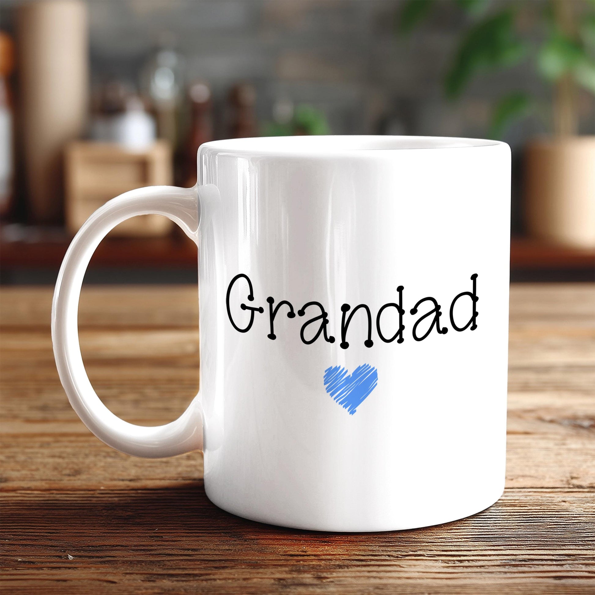 A white ceramic mug with the text "Grandad" and a blue heart symbol printed on it, placed on a wooden surface.