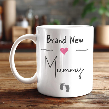 A white ceramic mug with the text "Brand New Mummy" printed on it, along with a heart symbol and baby footprints.