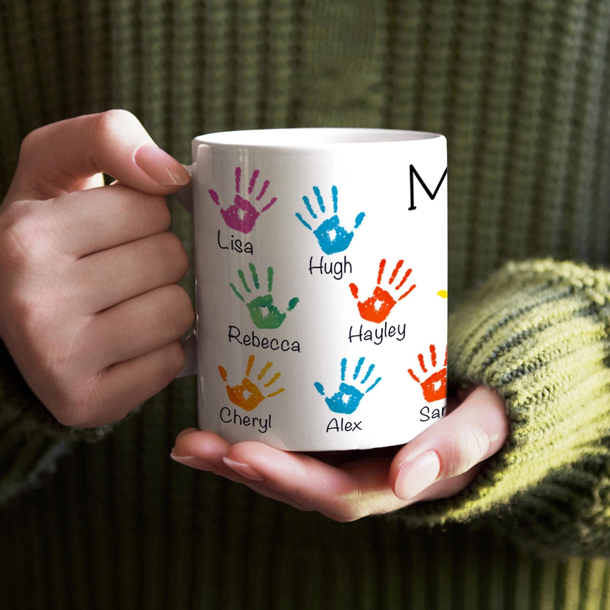 A person is holding a white mug with colorful handprints and names printed on it.