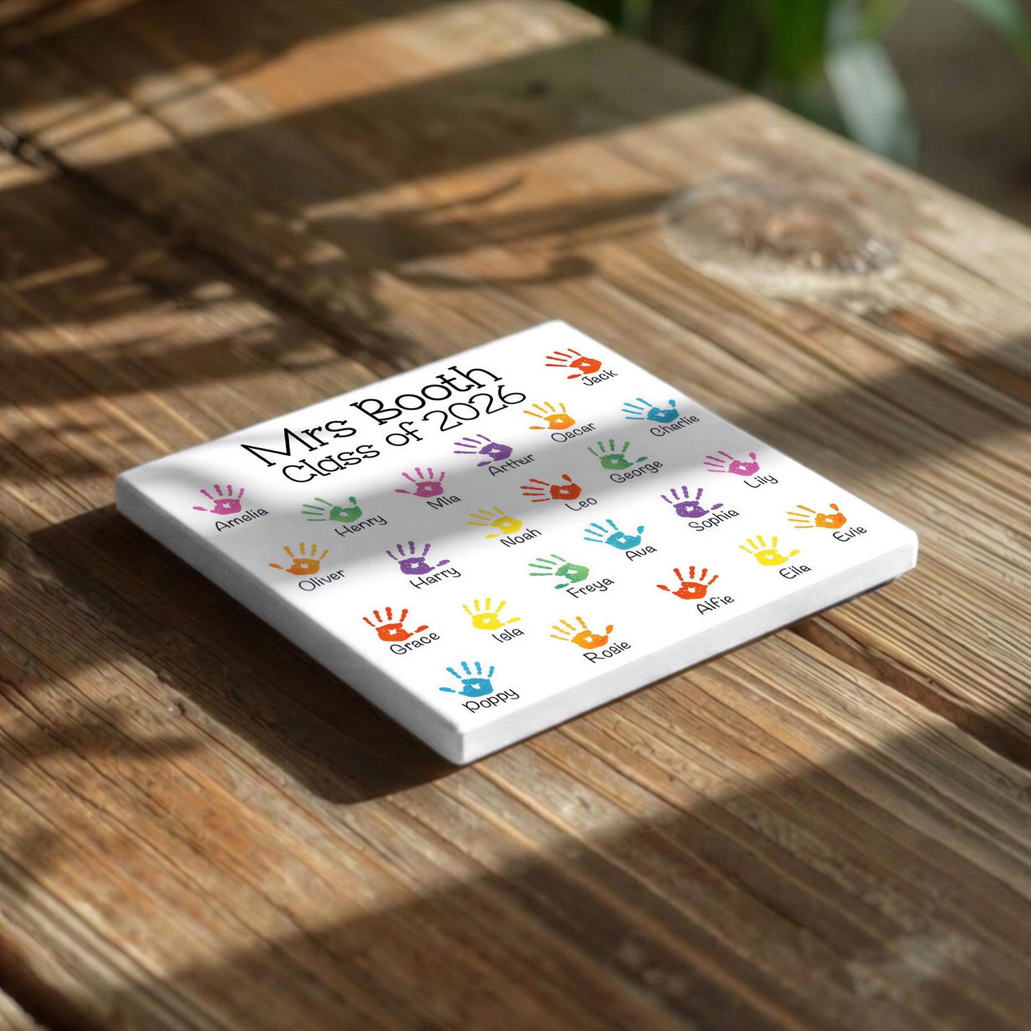 A white square with colorful handprint designs on it, placed on a wooden surface.
