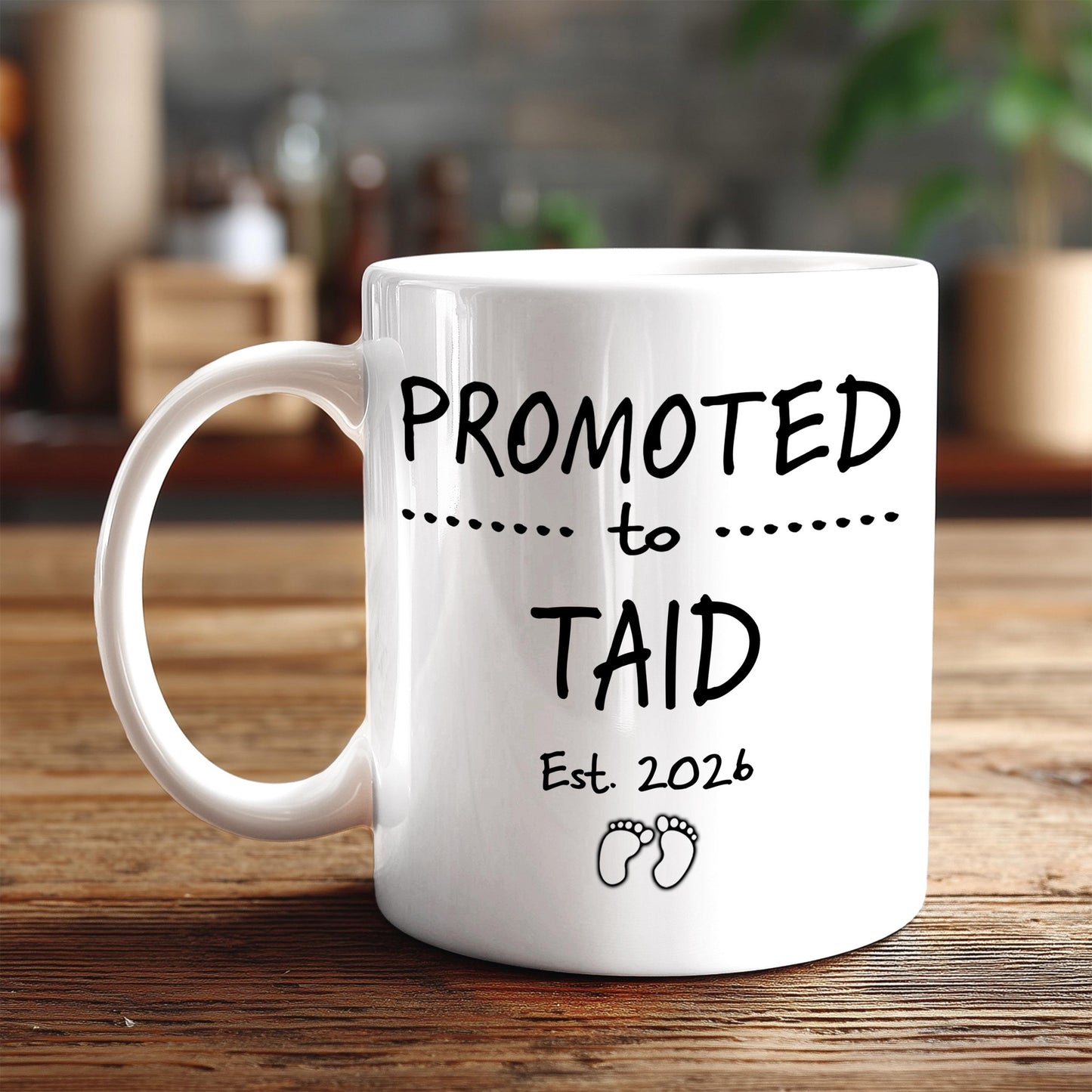 A white ceramic mug with the text "PROMOTED TO TAID Est. 2026" printed on it, along with a small illustration of a baby's feet.