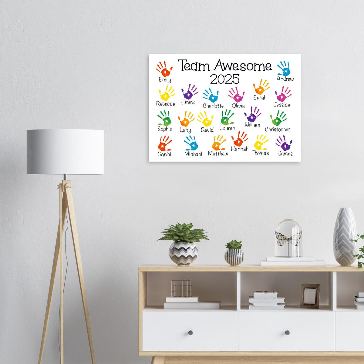 a colorful poster with handprints on it, hanging on a wall above a white cabinet with drawers.