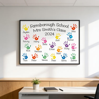 A framed poster with handprints on it, displaying the names of students in a class, and a plant on a desk in the foreground.
