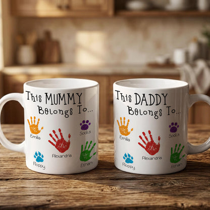 Two white mugs with handprint designs and names printed on them, placed on a wooden surface.
