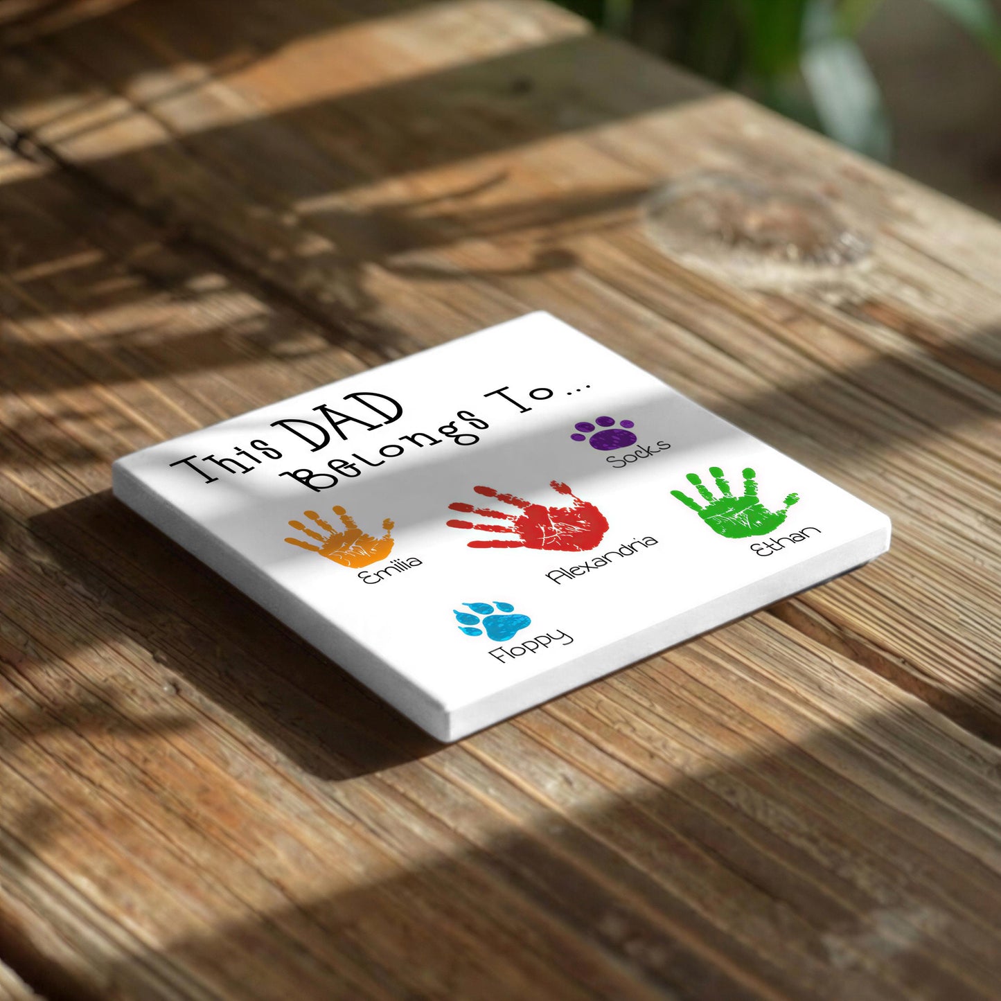 A white square canvas with handprints and names printed on it, placed on a wooden surface.