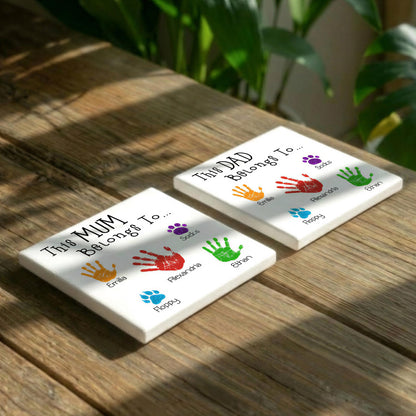 Two white coasters with handprint designs and text on them, placed on a wooden surface.