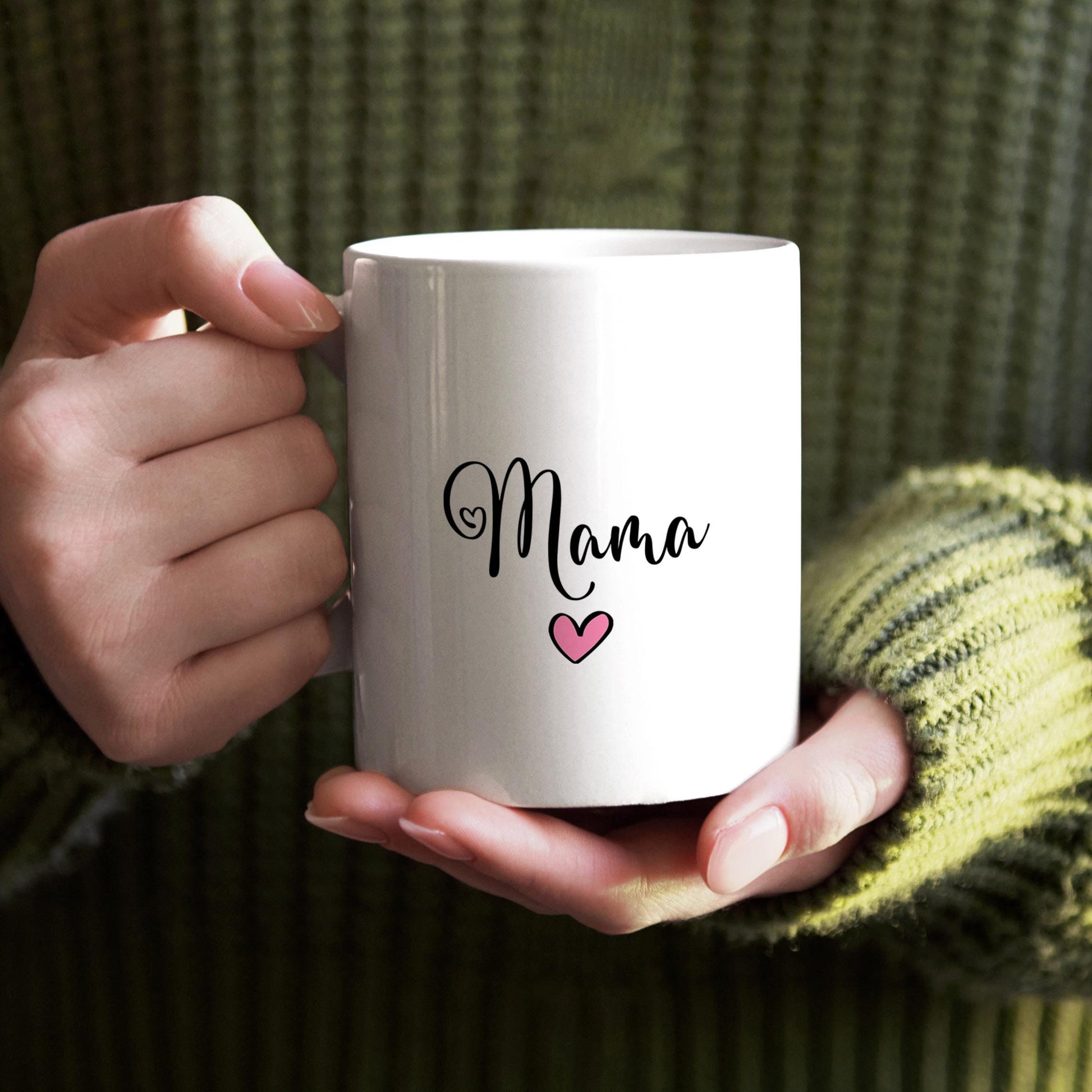 A person's hands holding a white mug with the word "Mama" and a heart symbol printed on it.