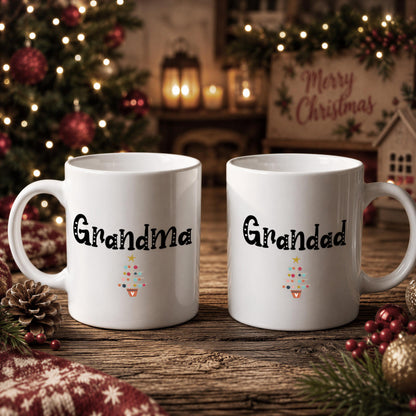 Two white mugs with the text "Grandma" and "Grandad" printed on them, placed on a wooden surface with Christmas decorations in the background.