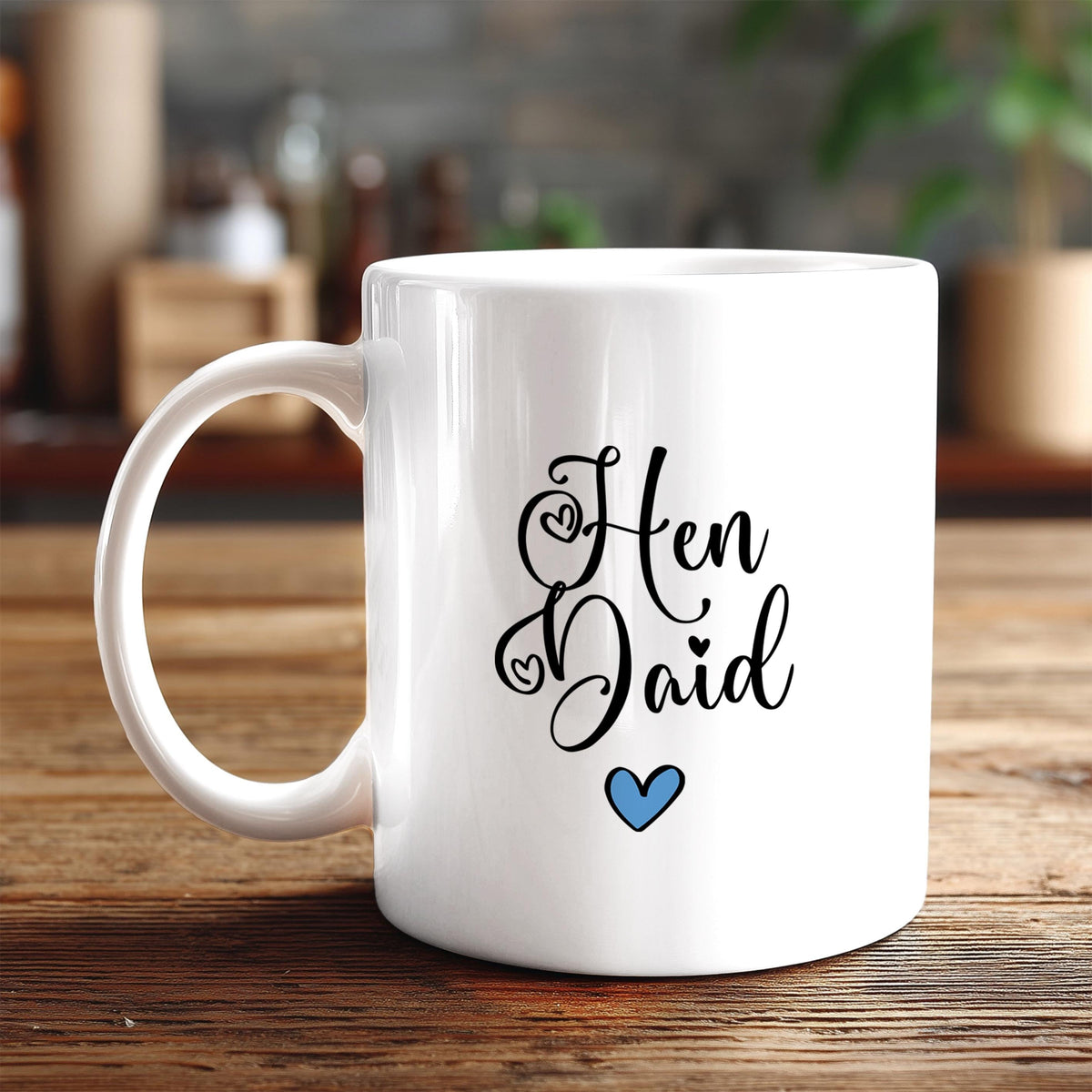 A white ceramic mug with the text "HEN DAID" and a blue heart symbol printed on it, placed on a wooden surface.