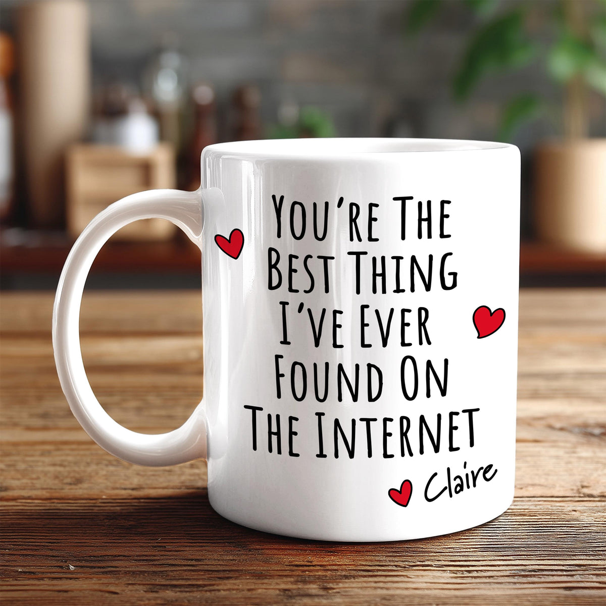 A white coffee mug with text printed on it, sitting on a wooden surface.