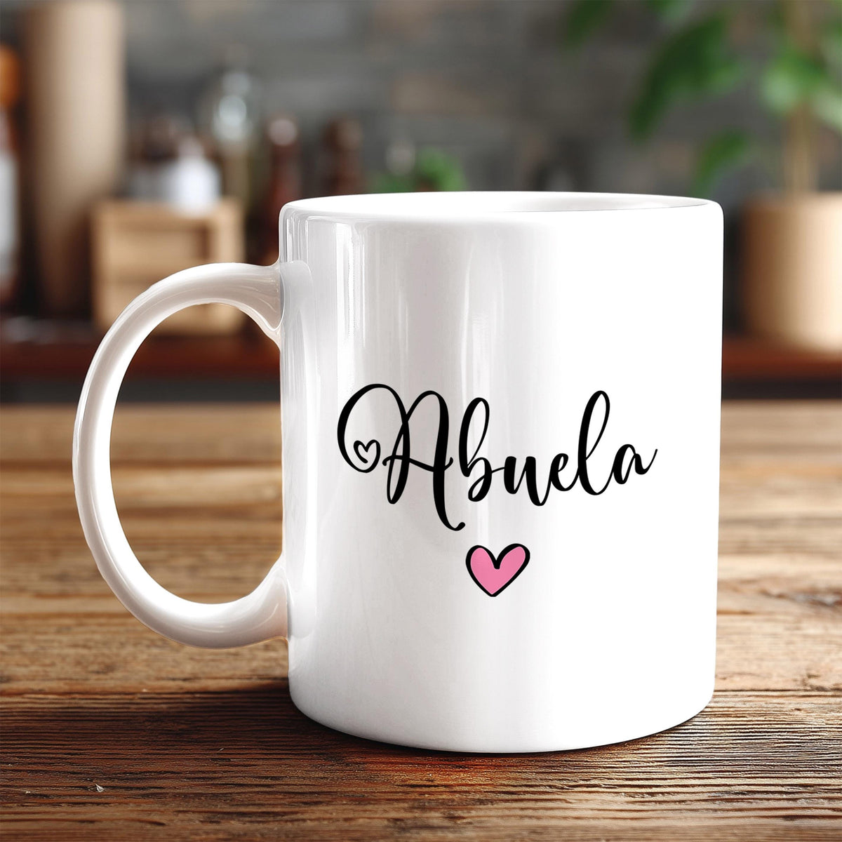 A white ceramic mug with the word "Abuela" written on it in cursive script, along with a small pink heart symbol.