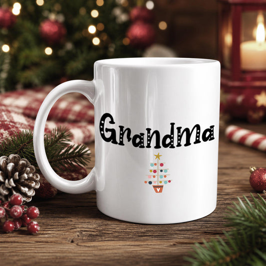 A white mug with the text "Grandma" printed on it, surrounded by Christmas decorations such as pine cones, ornaments, and a small Christmas tree.