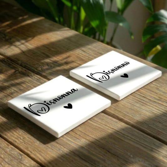Two white square coasters with the text "Wissenna" and two small heart symbols are placed on a wooden surface.