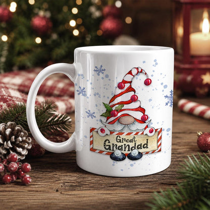 A white mug with a Christmas-themed design featuring a gnome wearing a red and white striped hat and the text "Great Grandad" on it, placed on a wooden surface with Christmas decorations in the background.