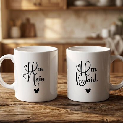 Two white mugs with black text and heart symbols, placed on a wooden surface.