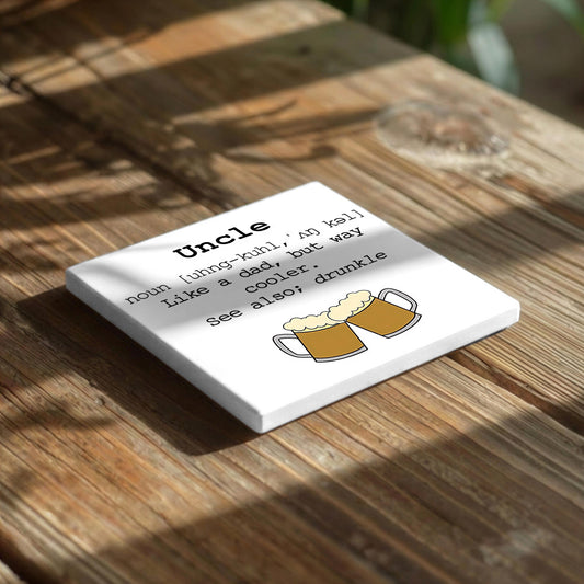 a white square coaster with a humorous definition of "Uncle" written on it, placed on a wooden surface.