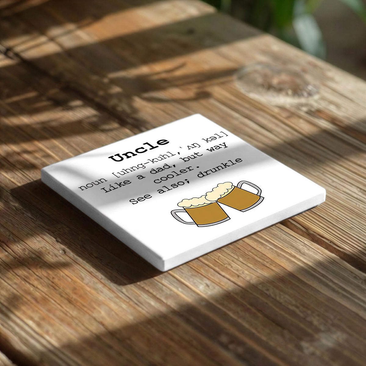 a white square coaster with a humorous definition of "Uncle" written on it, placed on a wooden surface.
