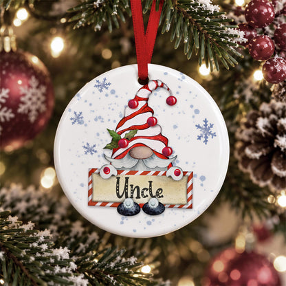 A white ornament with a red ribbon and a gnome design hangs on a Christmas tree, surrounded by snowflakes and ornaments.
