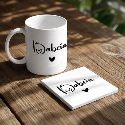 A white ceramic mug with the word "Abcia" printed on it, along with two small heart symbols, sits on a wooden table.