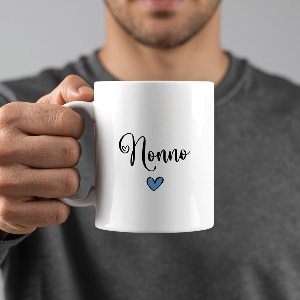 A person is holding a white mug with the word "Nonno" written on it, along with a small blue heart symbol.