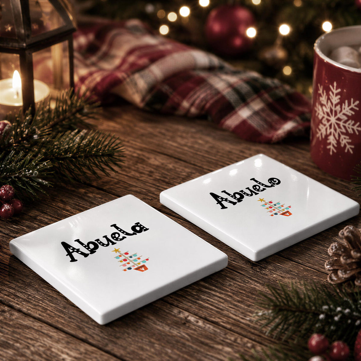 two white coasters with the name "Abuela" printed on them, placed on a wooden surface with a Christmas tree and other holiday decorations in the background.
