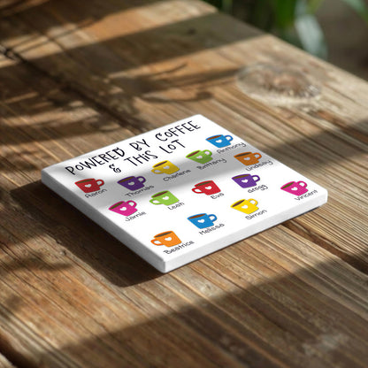 A white coaster with colorful coffee cup illustrations and text on it, placed on a wooden surface.