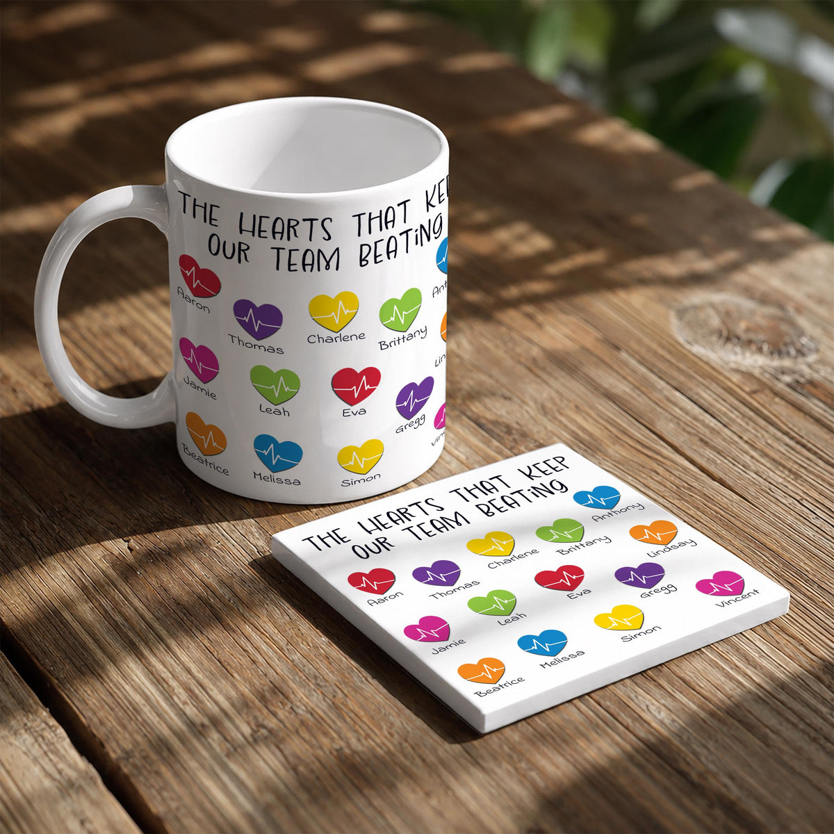 A white mug with a colorful design featuring heart shapes and text, and a coaster with heart shapes and text.