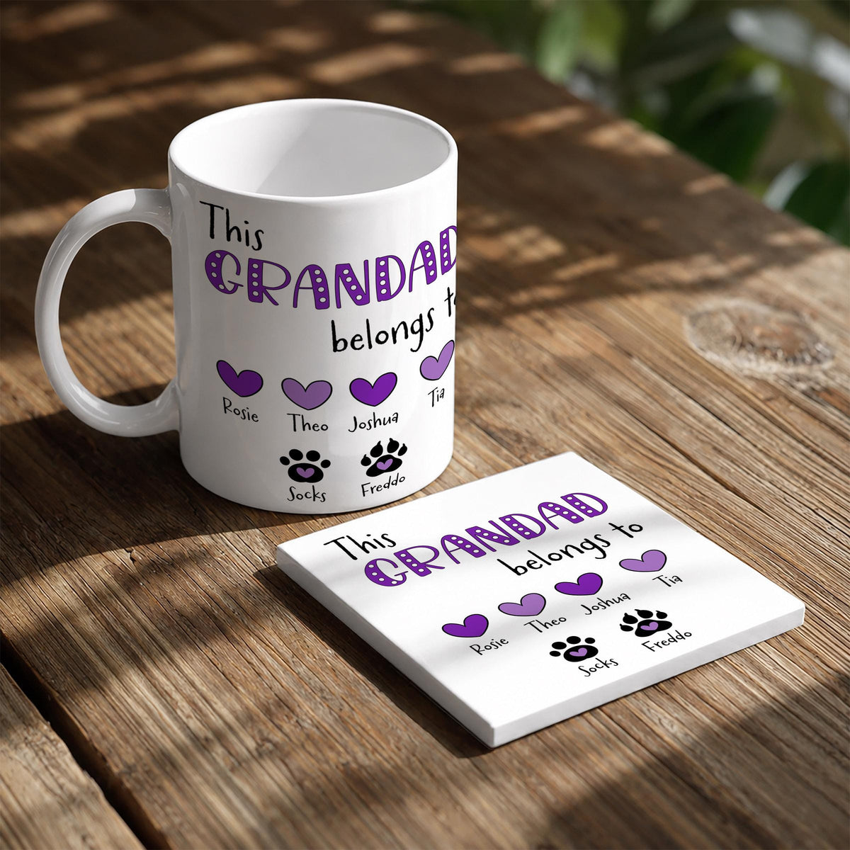 A white mug with purple text and a coaster with purple text are placed on a wooden table.