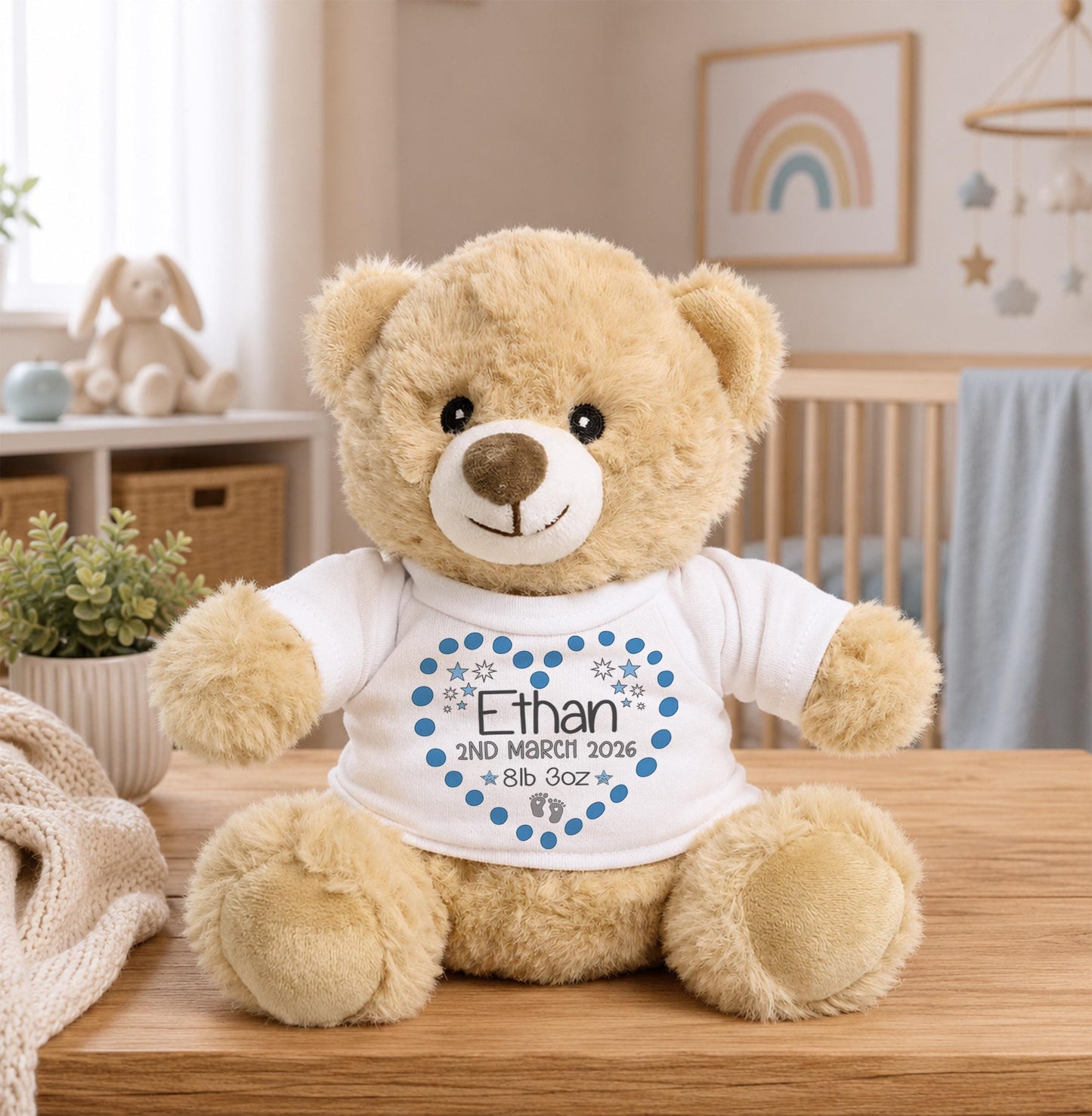 A brown teddy bear wearing a white shirt with a blue heart and the name "Ethan" printed on it, sitting on a wooden table in a nursery setting.