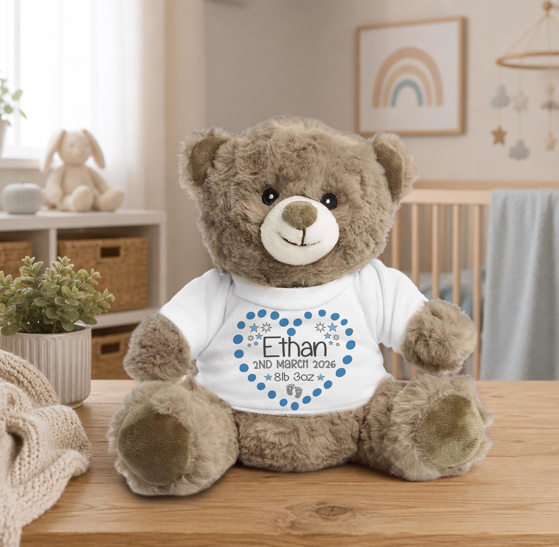 A brown teddy bear wearing a white t-shirt with a blue heart and the name "Ethan" printed on it, sitting on a wooden table.