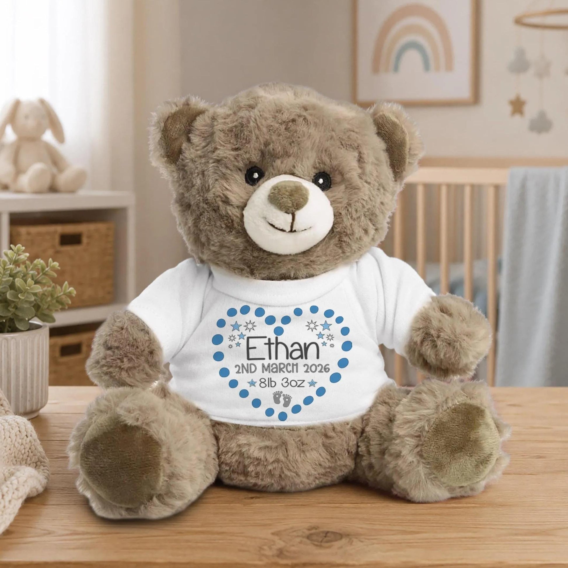 A brown teddy bear wearing a white t-shirt with a blue heart and the name "Ethan" printed on it, sitting on a wooden table.