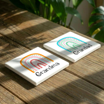 Two white coasters with colorful rainbows and the text "Grandma" printed on them, placed on a wooden surface.