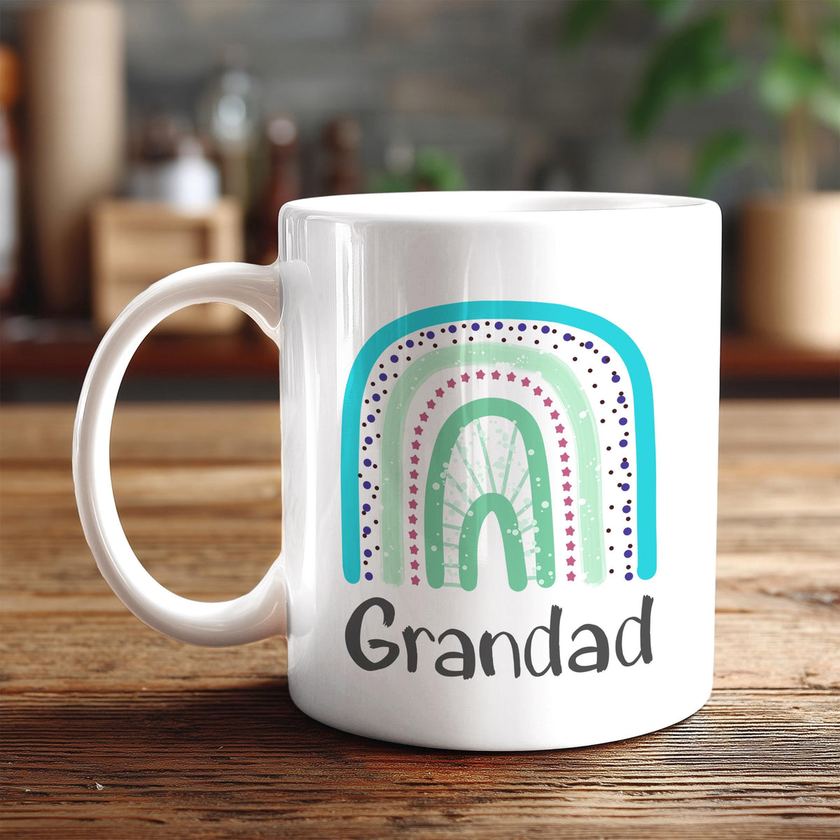 A white ceramic mug with a colorful rainbow design and the word "Grandad" printed on it, placed on a wooden surface.