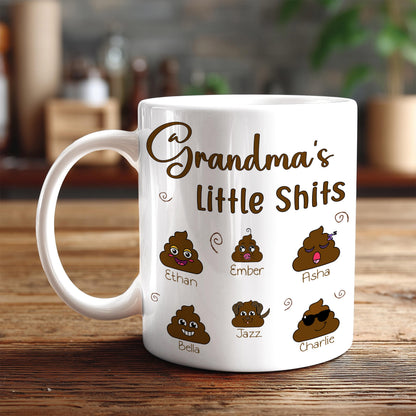 A white coffee mug with a humorous design featuring cartoon-style poop faces and names, along with the text "Grandma's little shit".