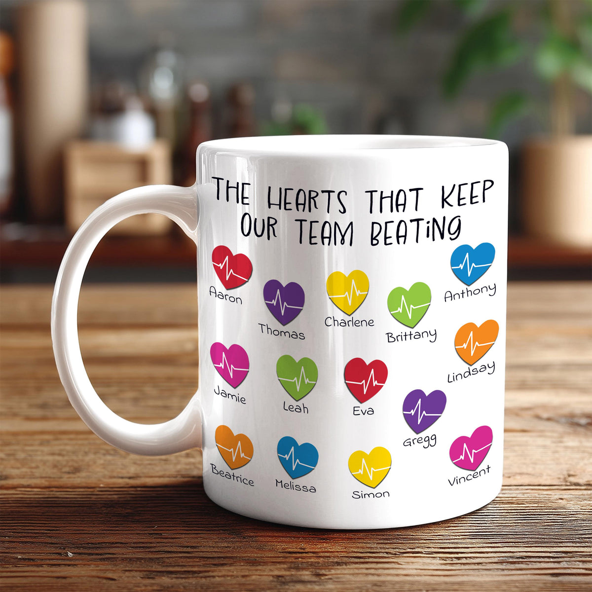 A white mug with a printed message that reads "The hearts that keep our team beating" along with various heart icons representing different people.