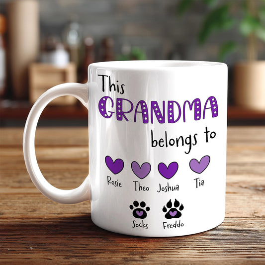 A white mug with a personalized message that reads "This Grandma belongs to Rosie, Theo, Tia, Socks, Fredo" along with three heart symbols and paw prints.