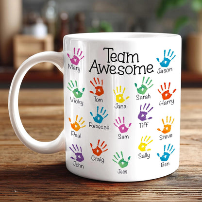 A white mug with colorful handprints on it, each containing a name.